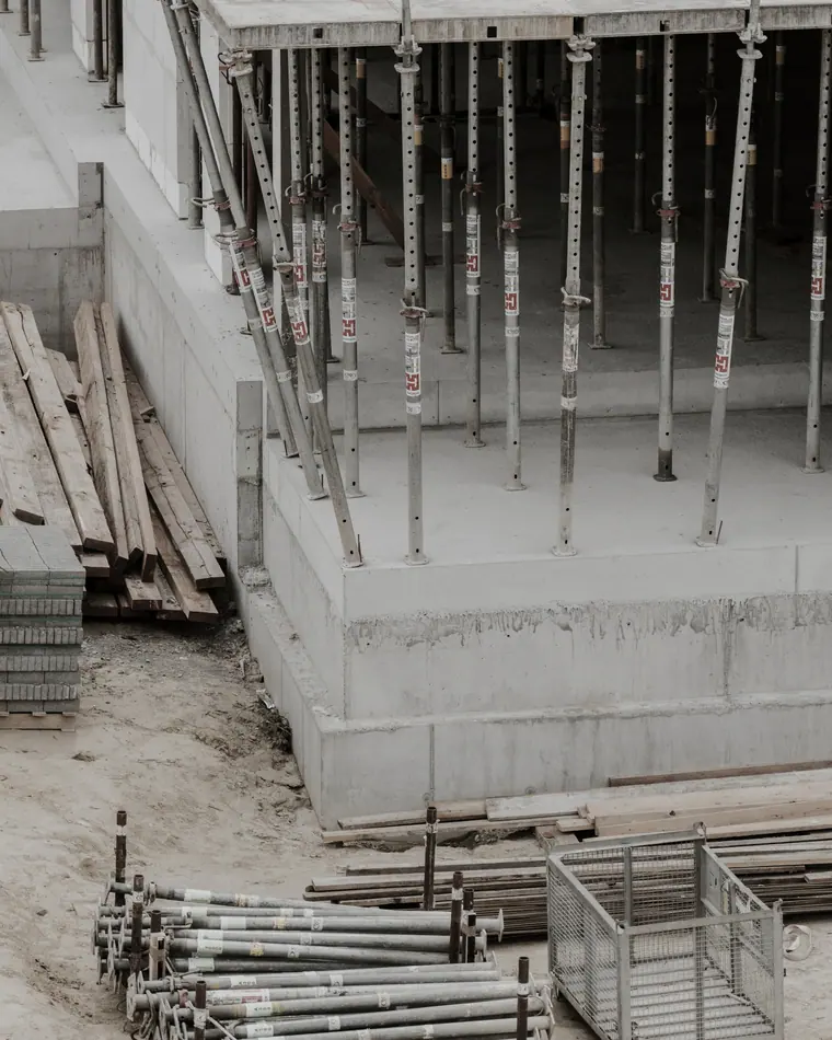 Escoras metálicas apoiando uma laje recém-concretada, com tábuas de fôrma ao lado.