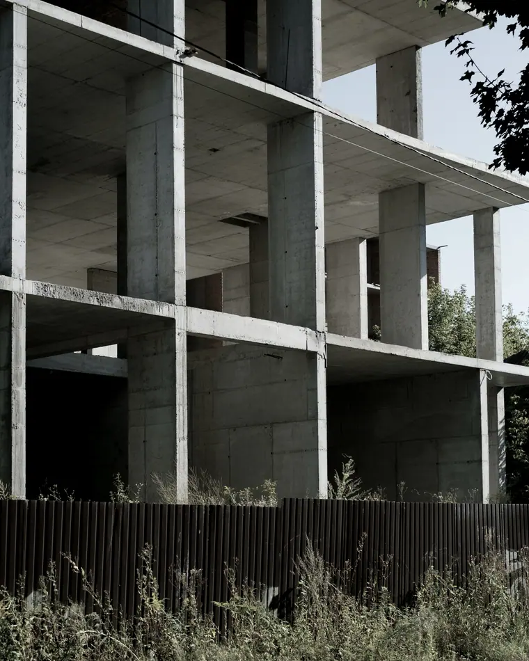 Pórtico de concreto armado de uma edificação em construção, visto através de um tapume.