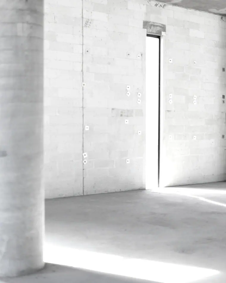 Interior de concreto ainda em obra bruta, iluminado por uma abertura vertical.