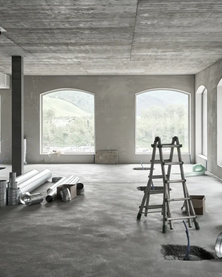 Sala ampla em reforma, com escada de pintor, material no chão e janelas em arco.